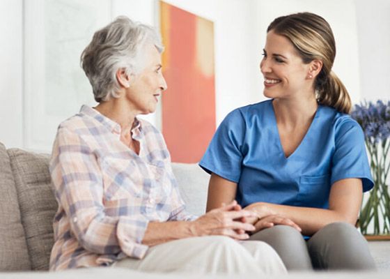 Nurse Sitting with Elderly Woman on Couch Offering In-Home Care Services in Concord, NH