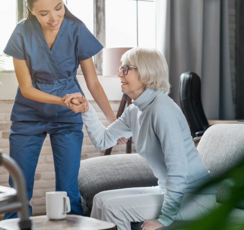Nurse Helping Elderly Lady Stand Up from Couch Assisting with In-Home Care Services in Concord, NH