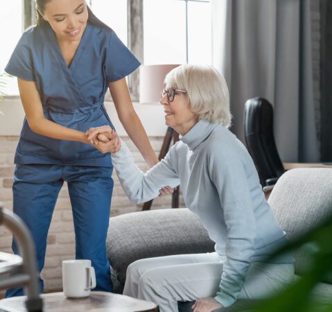 Caregivers for Seniors Concord, NH, assisting an elderly woman up from a couch